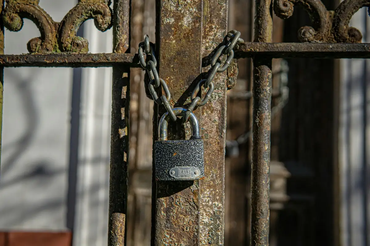 Grille en fer forgé gagnée par la rouille, fermée par une chaîne et un cadenas