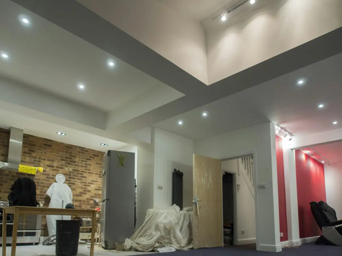 Pièce en travaux : mur de briques apparent, spots posés au plafond, mobilier bâché